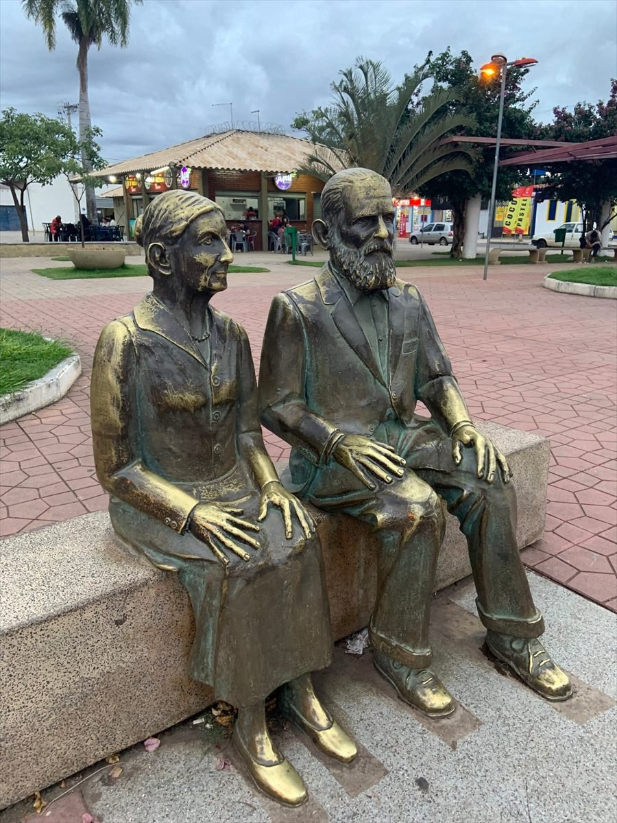 Casal de idosos em bronze sentado em banco de praça