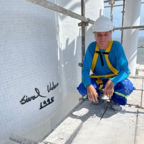 Sival Veloso no ateliê, ao lado de sua assinatura em uma obra